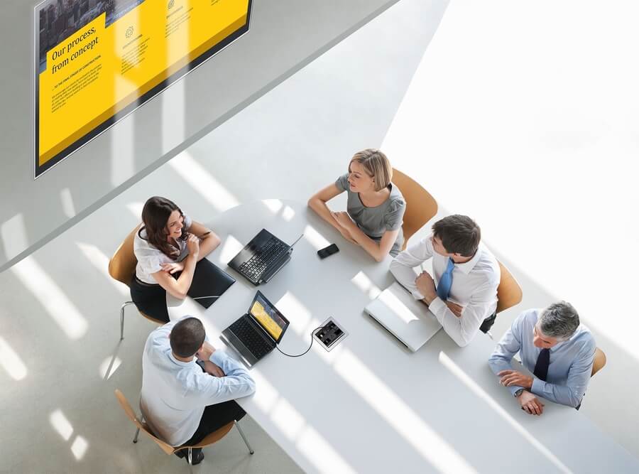 Overhead shot of people at a white conference room table using audio visual hardware.