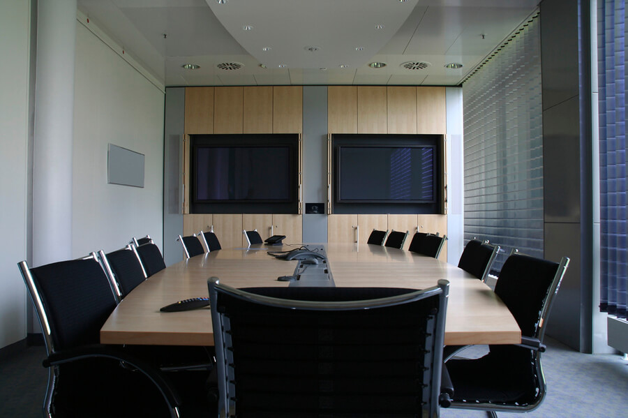 Conference room with two TV screens, a large wood table, and 13 black seats.