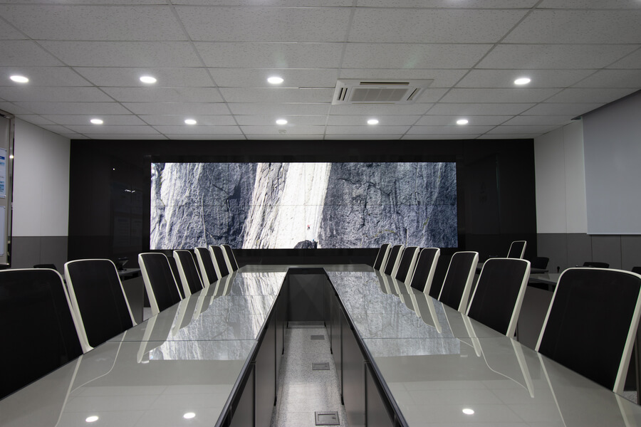 A conference room with two tables facing each other and a large video wall display.