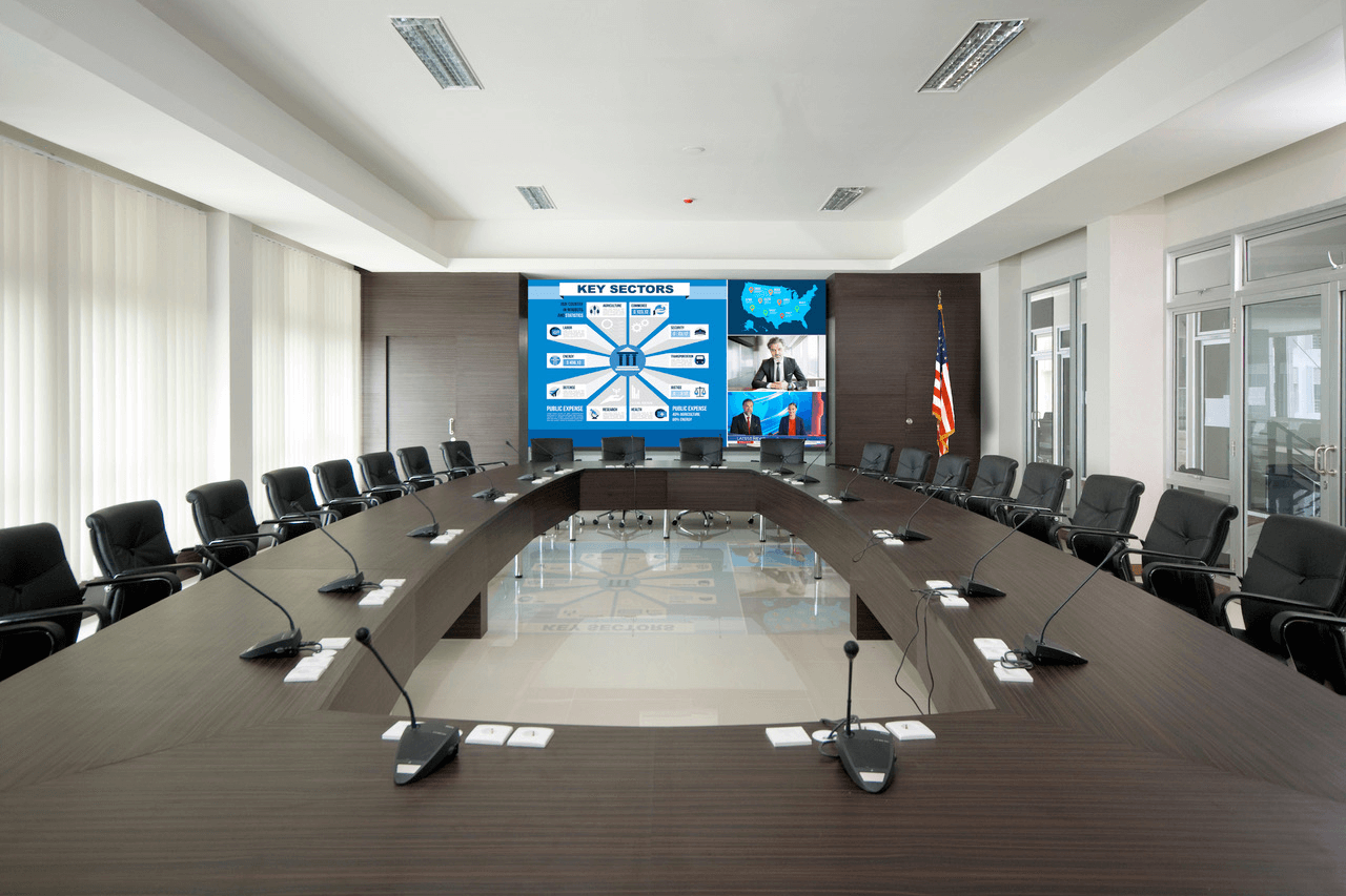 A boardroom with a large video display and microphones at every seat.